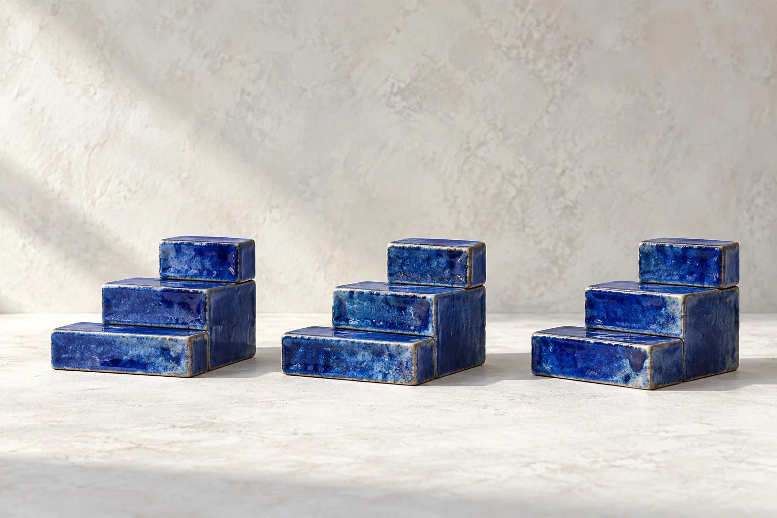 Cobalt ceramic blocks form modest repeating steps on a pale textured surface in gentle daylight.