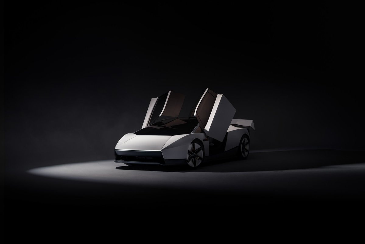 A white, sharply angular open-top roadster, both doors raised, on a dark studio floor.