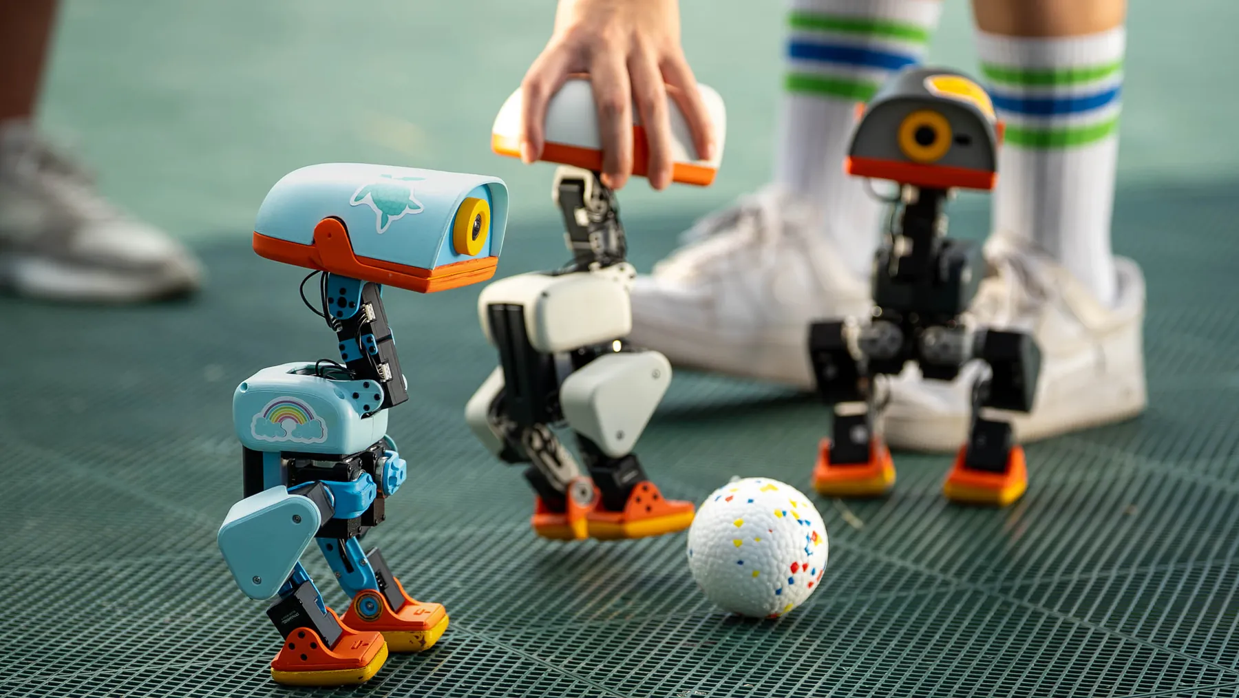 Two Microduck robots playing with a ball on green turf