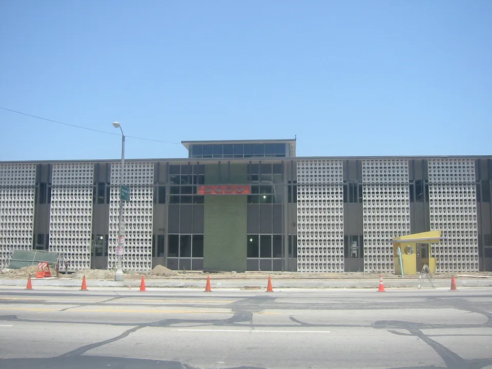 Mid-century studio facade with geometric concrete screens, central glass entrance and traffic cones along the street.