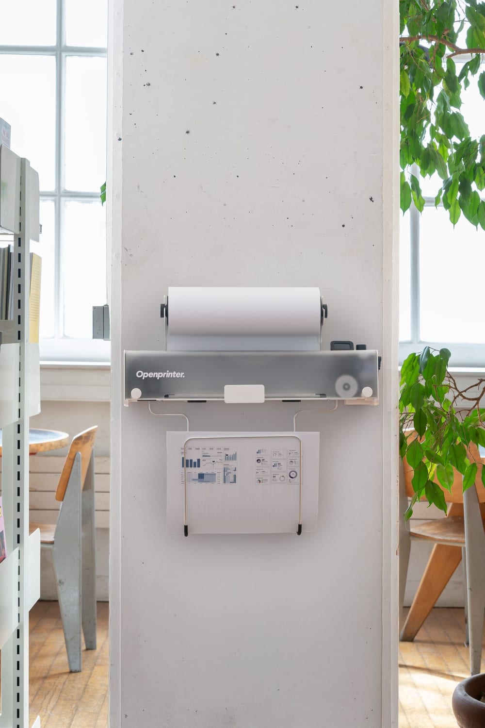 Openprinter mounted on a white column with a roll on top and a printed chart hanging in a wire tray below