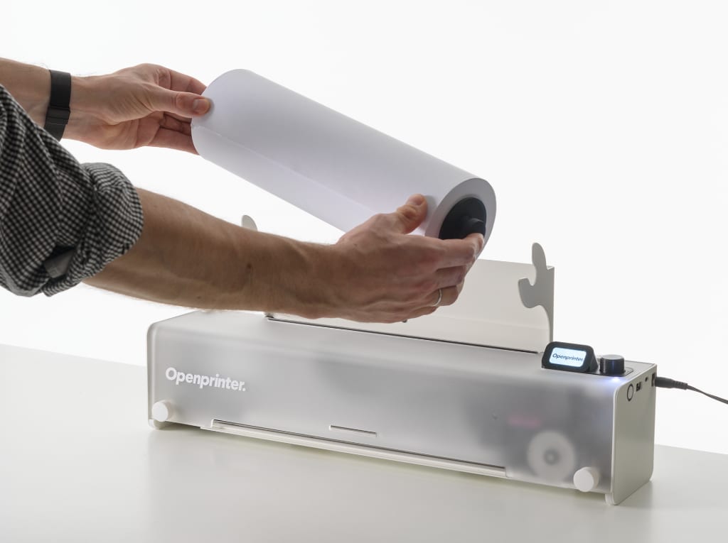 Hands lifting the paper roll off the top of the Openprinter to load sheets
